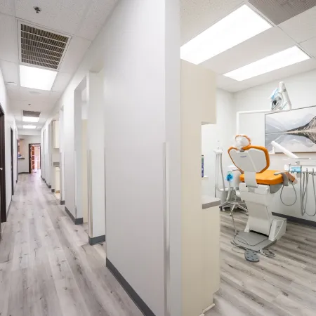 Modern dental clinic hallway with treatment rooms featuring orange dental chairs and clean white interiors.