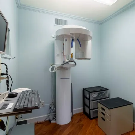 Dental 3D X-ray machine in a small room with light blue walls and computer workstation.