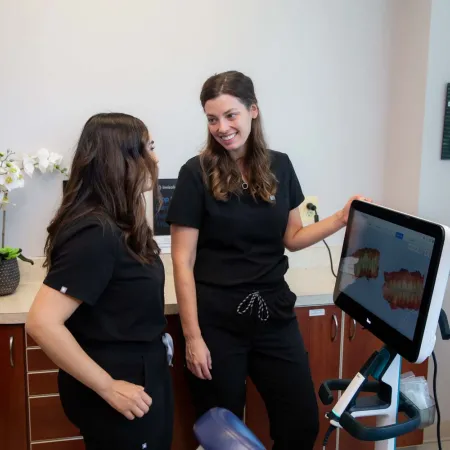 Two dental professionals in black scrubs discussing 3D dental images displayed on a computer screen in a clinic.