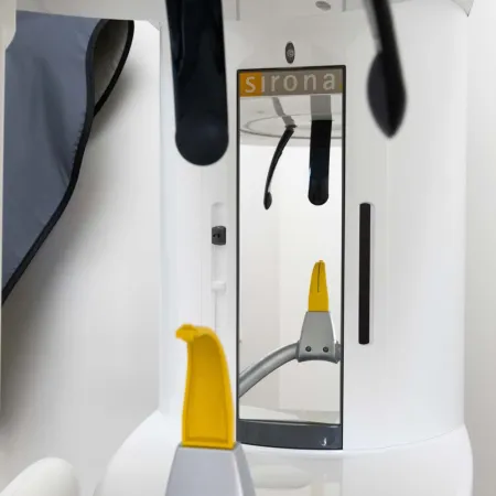 Close-up of Sirona dental imaging machine with yellow headrest and reflective surfaces in clinical setting