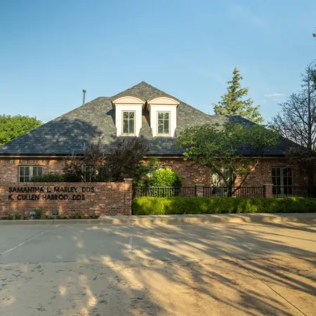 Brick dental office building with parking lot, trees, and sunny blue sky in suburban setting