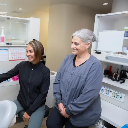 Dental professional explaining Invisalign options to a smiling patient using a touchscreen display in clinic.