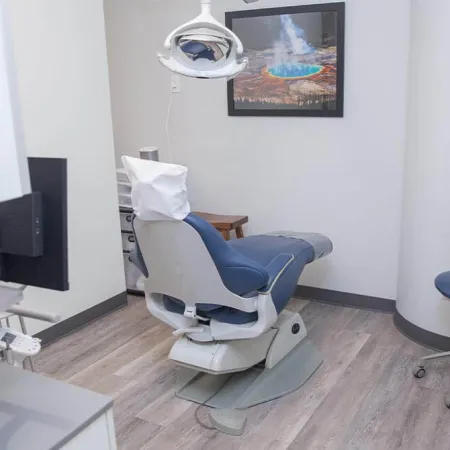 Modern dental office with adjustable chair, blue stools, overhead light, and framed nature artwork on wall
