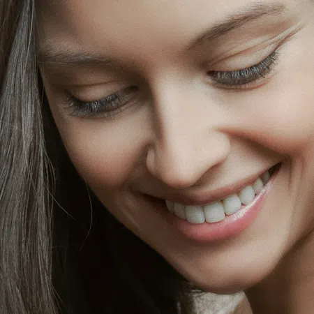 Close-up of a smiling woman's face with long brown hair and clear skin, conveying happiness and warmth.