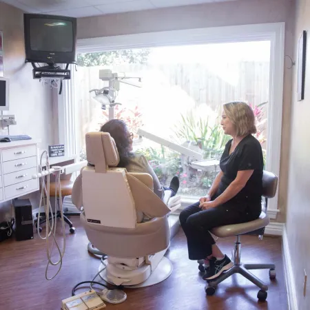 Dentist consulting patient in bright dental office with large window and modern equipment.