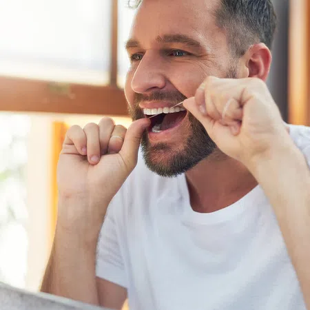 Man flossing his teeth at home in a well-lit bathroom, focusing on dental hygiene.
