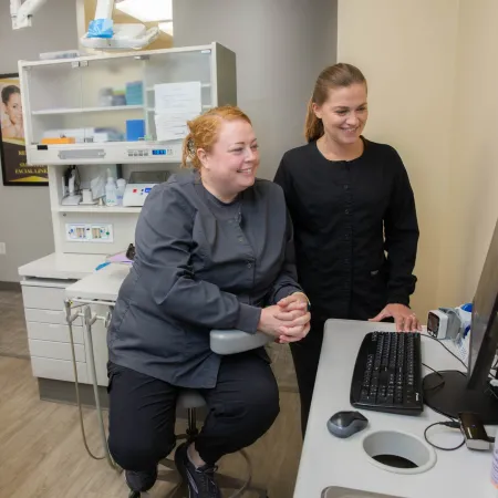 Two dental professionals review patient information on a computer in a modern dental office setting.