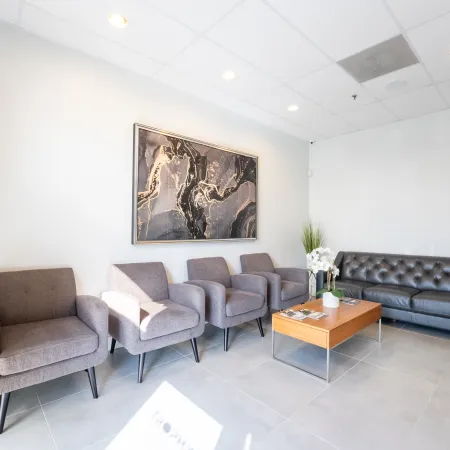 Modern waiting room with gray armchairs, black leather sofa, wooden coffee table, and abstract wall art.