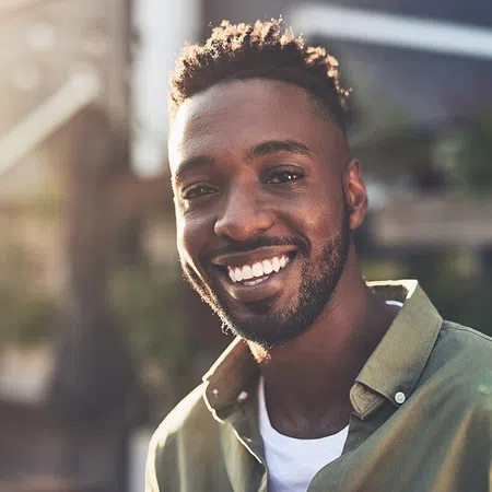 Smiling man outdoors in natural light, wearing a casual shirt, showcasing positive attitude and warmth.