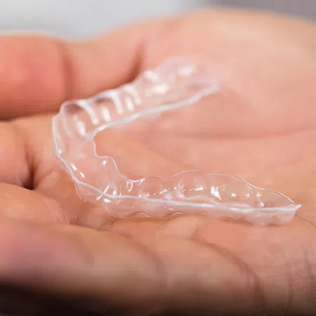 A person holding a clear dental retainer in their hand, showcasing its transparent design.