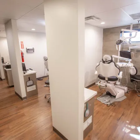 Modern dental office with treatment chairs, equipment, bright lighting, and wooden flooring in private rooms.