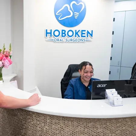 Young male patient speaking with a smiling receptionist at Hoboken Oral Surgeons front desk with flowers in background