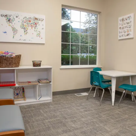 Cozy kids' play area with small white table, two blue chairs, bookshelf, and colorful wall maps.