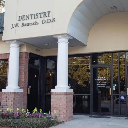 Entrance to J.W. Bautsch DDS dentistry office with pillars, brick exterior, flowers, and glass doors.