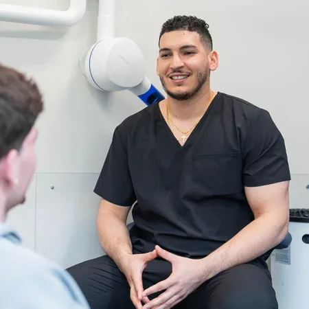 Dentist in black scrubs talking to a patient seated in a dental chair in a modern clinic.