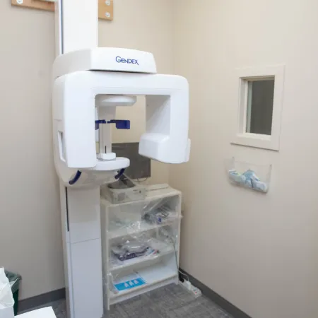 Gendex dental panoramic X-ray machine in a clean medical room with equipment and supplies.