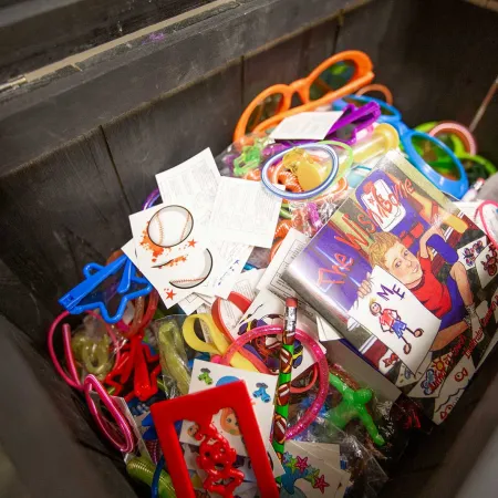 Box filled with colorful party favors, cards, glow sticks, and playful toys including glasses and drawing books.