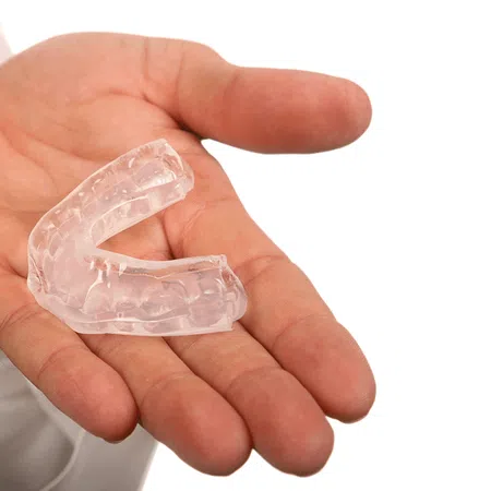 A person holding a clear dental mouthguard in an open hand against a white background.
