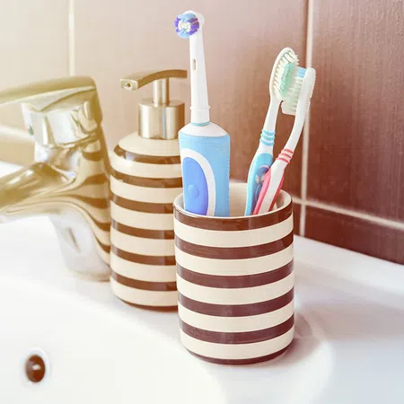 Stylish bathroom accessories with striped holder, toothbrushes, and electric toothbrush near faucet.