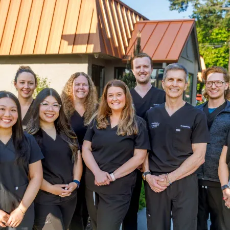 Group of smiling medical professionals in black scrubs posing outdoors in front of a building with copper roof.