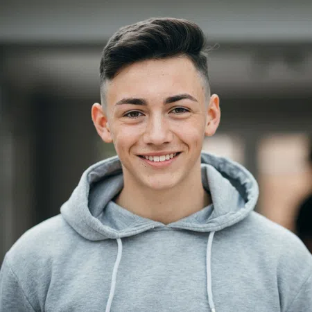 Smiling young man in a gray hoodie, indoors with a blurred background of people.