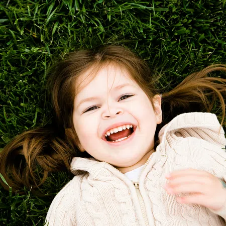 Happy young girl with pigtails lying on green grass smiling and laughing outdoors