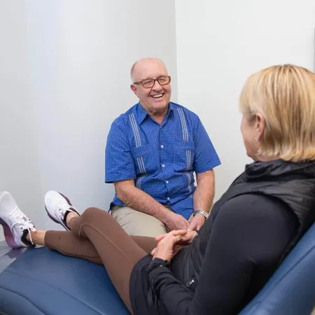 Senior man smiling and talking with a woman lying on a medical exam table in a clinic room