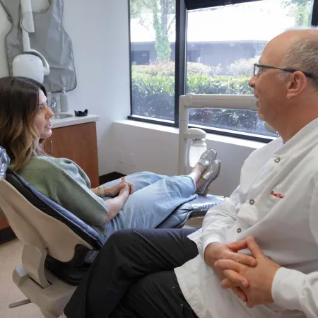Dentist consulting with female patient sitting in dental chair in a bright office with window view.