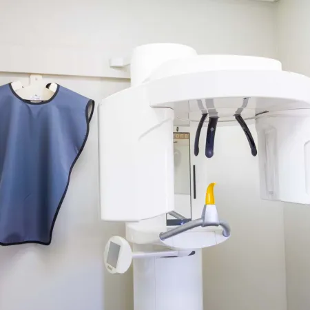 Dental x-ray machine next to a blue lead apron hanging on a white wall in a dental clinic.