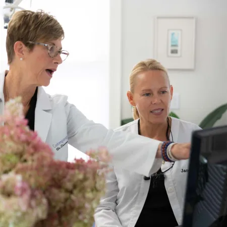 Two female doctors in white coats reviewing medical images on a computer screen in a bright office.