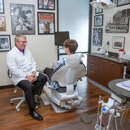 Dentist in white coat consulting young male patient seated in dental chair in modern office