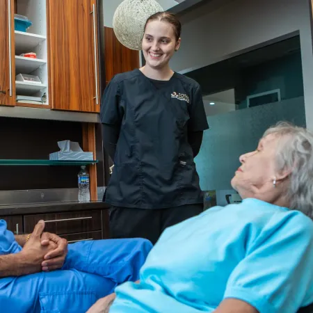 Dentist consulting elderly female patient in dental office with assistant smiling in background