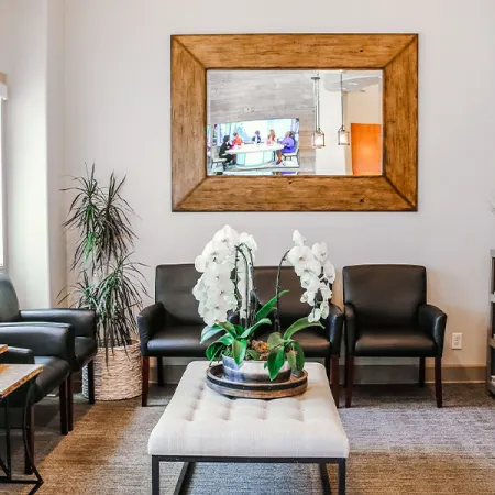 Stylish waiting room with modern furniture, plants, and framed mirror, creating a welcoming atmosphere.