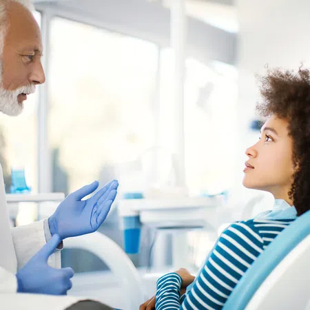 A dentist consults a young woman in a bright dental clinic, discussing treatment options.