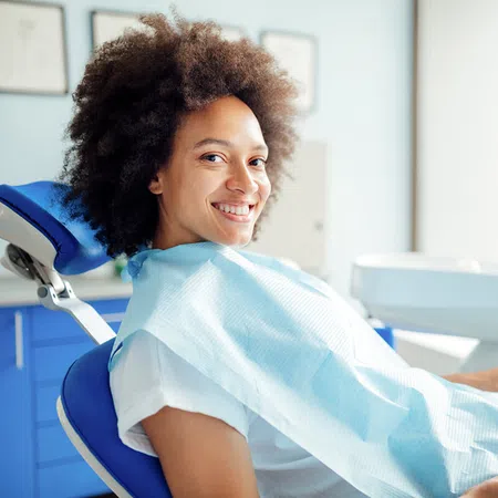 Smiling woman sitting in a dental chair with a dental bib in a bright clinic.