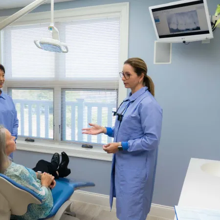 Dentist and assistant discussing treatment with patient in modern dental office with blue decor.