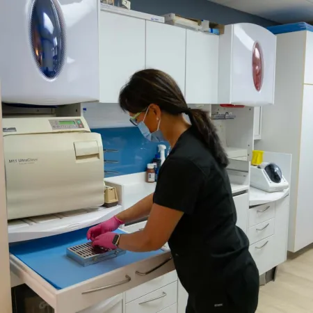 Dental professional wearing gloves and mask operating sterilization equipment in a clean clinic workspace