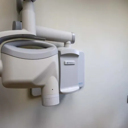Wall-mounted dental X-ray machine in a clinical setting with beige walls and minimal background details.