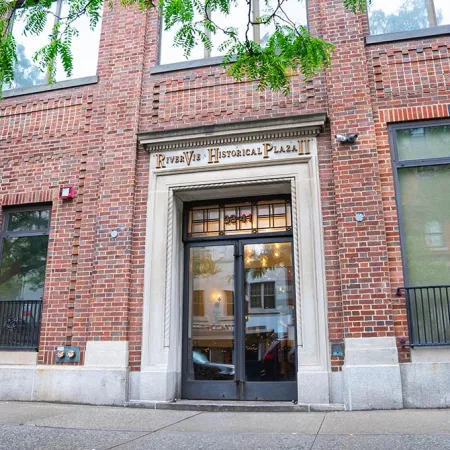 Entrance to River Vue Historical Plaza with brick facade, large windows, and glass double doors beneath a stone marquee.