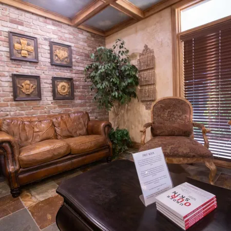 Cozy waiting room with leather sofa, patterned armchair, brick wall, indoor plant, and wooden blinds with soft lighting.