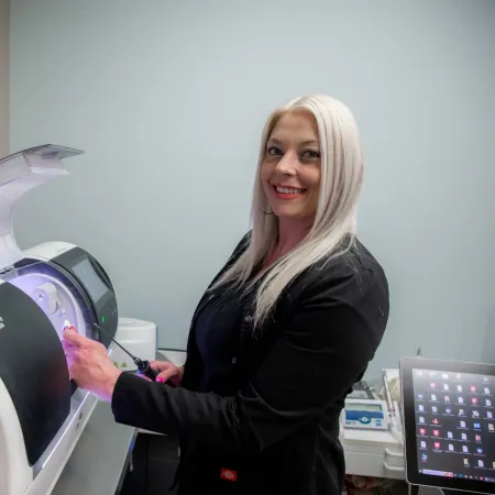 Smiling woman operating a modern dental milling machine in a clean dental laboratory setting.