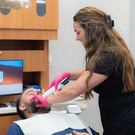 Dental professional wearing pink gloves using intraoral scanner on male patient in dental office