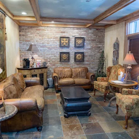Cozy living room with leather sofas, floral armchairs, brick wall, and warm lighting from table lamps