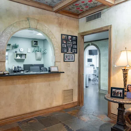 Cozy waiting room with stone floor, arched reception window, leather chair, and decorative lamp on side table.