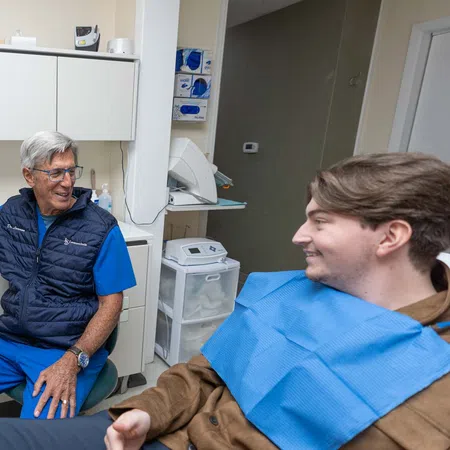 Senior male dentist explaining dental X-ray results to a young male patient in a modern dental clinic.