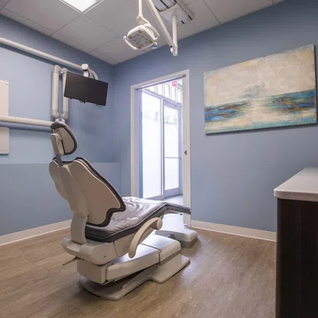 Modern dental office with patient chair, wall-mounted monitor, medical equipment, and calming blue walls with artwork.