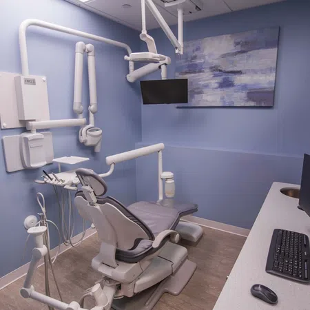 Modern dental office with a dental chair, overhead light, monitor, and computer workstation against blue walls.