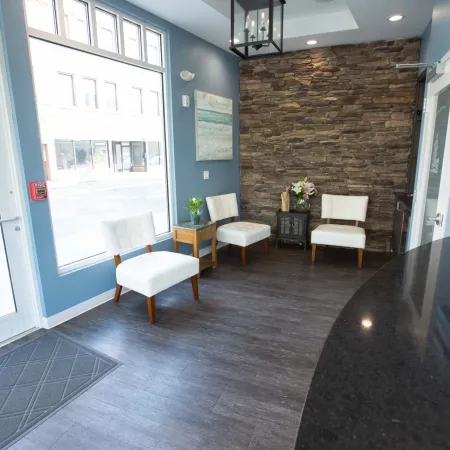 Bright waiting room with blue walls, white chairs, stone accent wall, and granite reception desk.