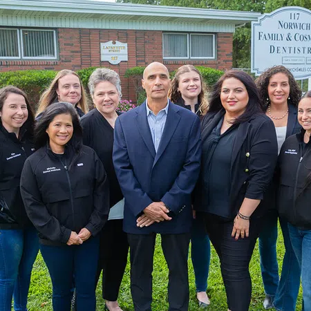 Group of dental professionals posing outside Norwich Family & Cosmetic Dentistry building on grassy lawn.