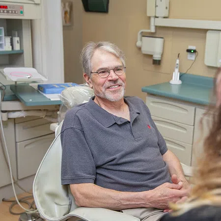 Smiling elderly man sitting in dental chair talking to a female dental professional in a clinic